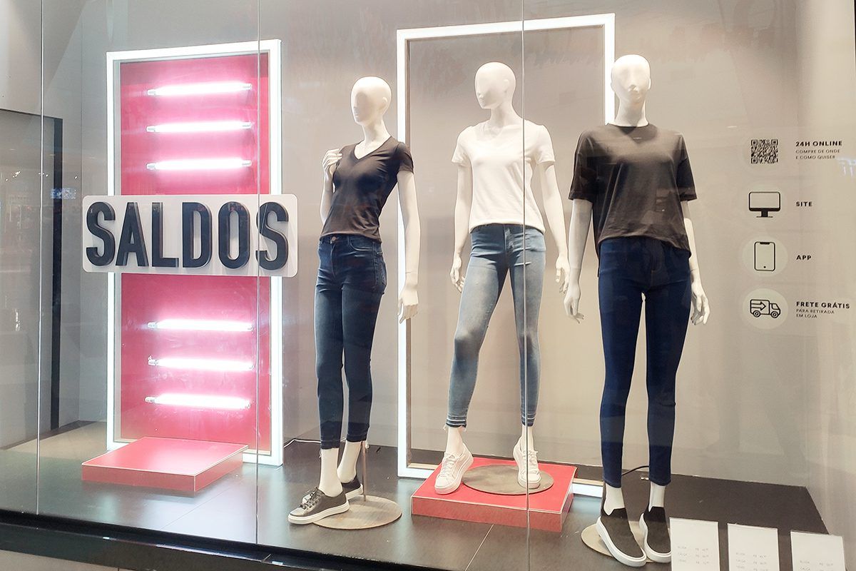 Imagem de vitrine de loja do Shopping Jardins com três manequins vestindo jeans e camiseta e a palavra Saldos