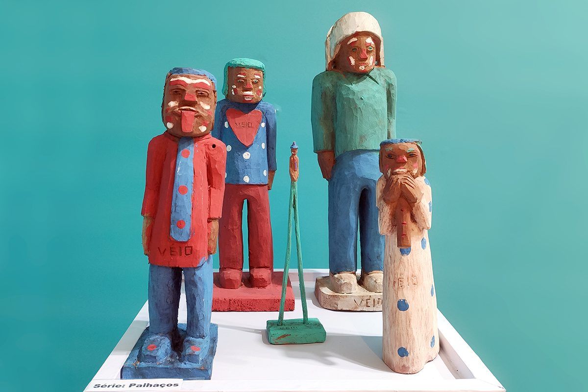 Imagem com cinco esculturas coloridas em madeira da série Palhaços, criada pelo artista popular Véio
