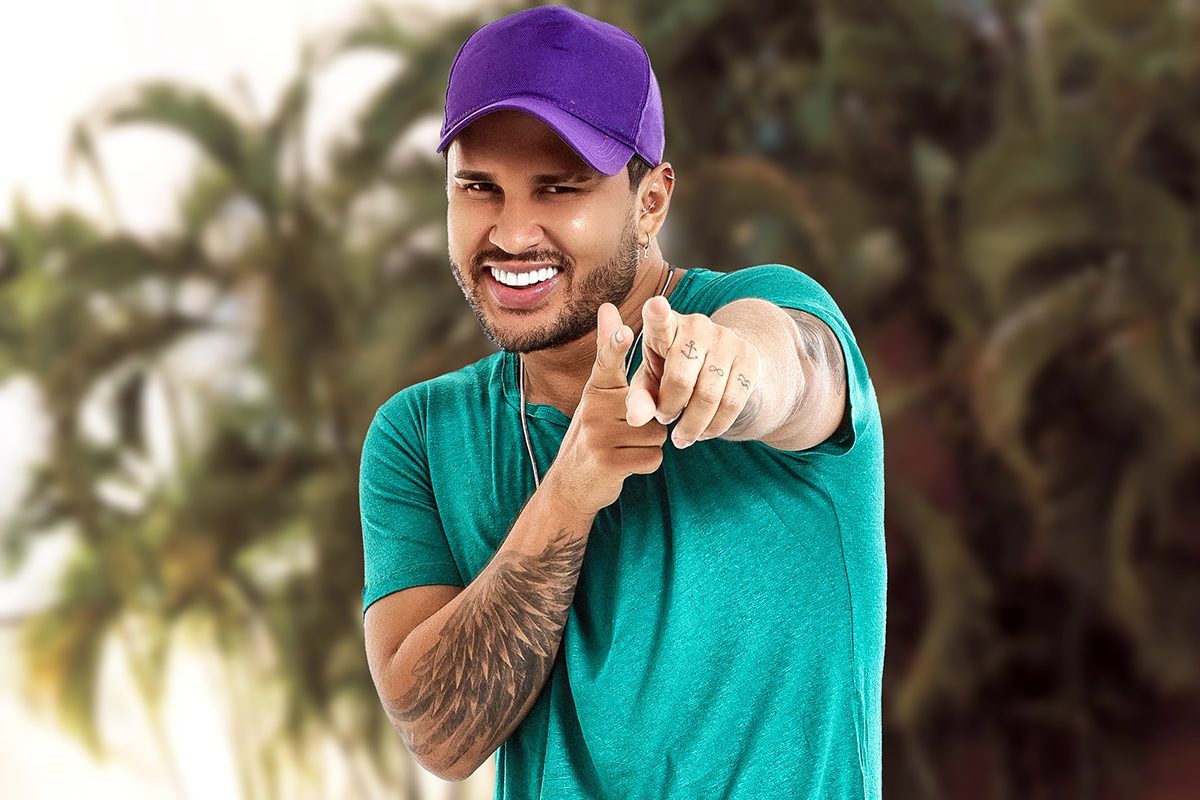 Imagem de Lucas Guimarães, de boné azul e camisa verde, sorrindo e apontando para o espectador