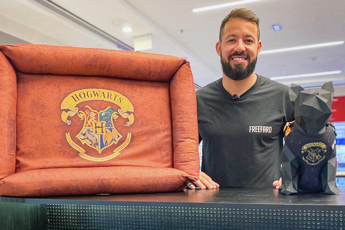 Foto do empresário Rennan Albuquerque vestindo camisa preta com o nome FreeFaro, dentro do quiosque da marca ao lado de uma cama para cachorros com estampa do Harry Potter, representando um dos produtos do mercado pet