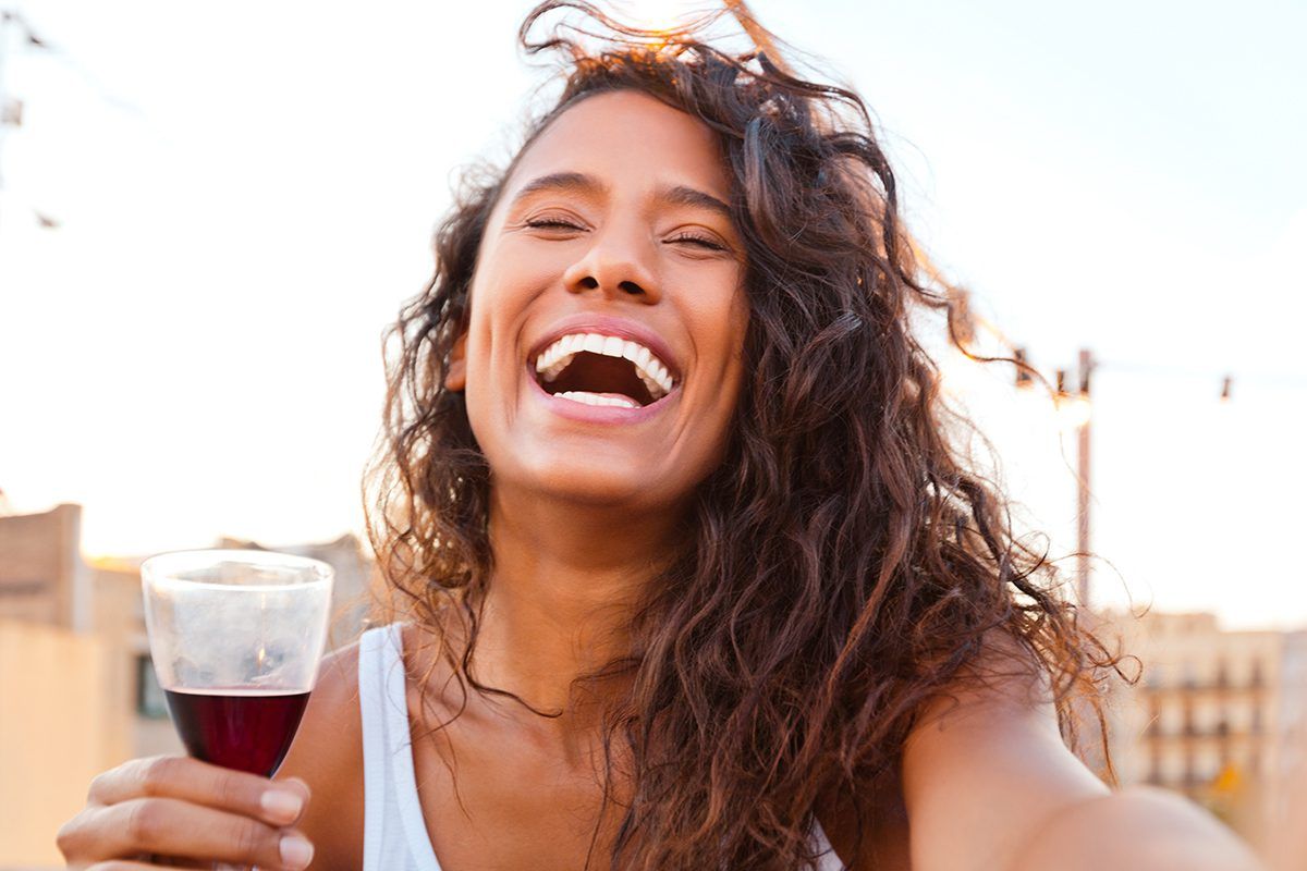 Imagem de mulher sorrindo com taça de vinho tinto na mão