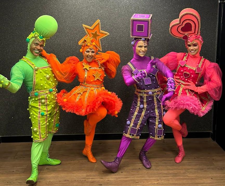 Imagem de quatro personagens sorrindo, vestindo roupas coloridas